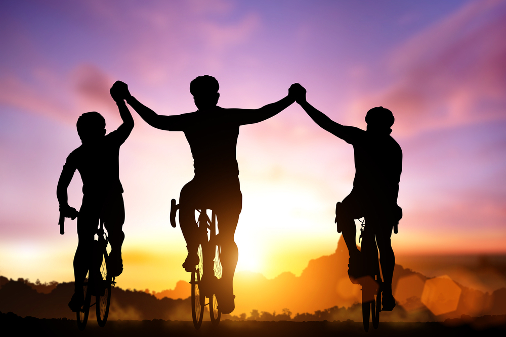 Three cyclists on bikes hold hands in silhouette